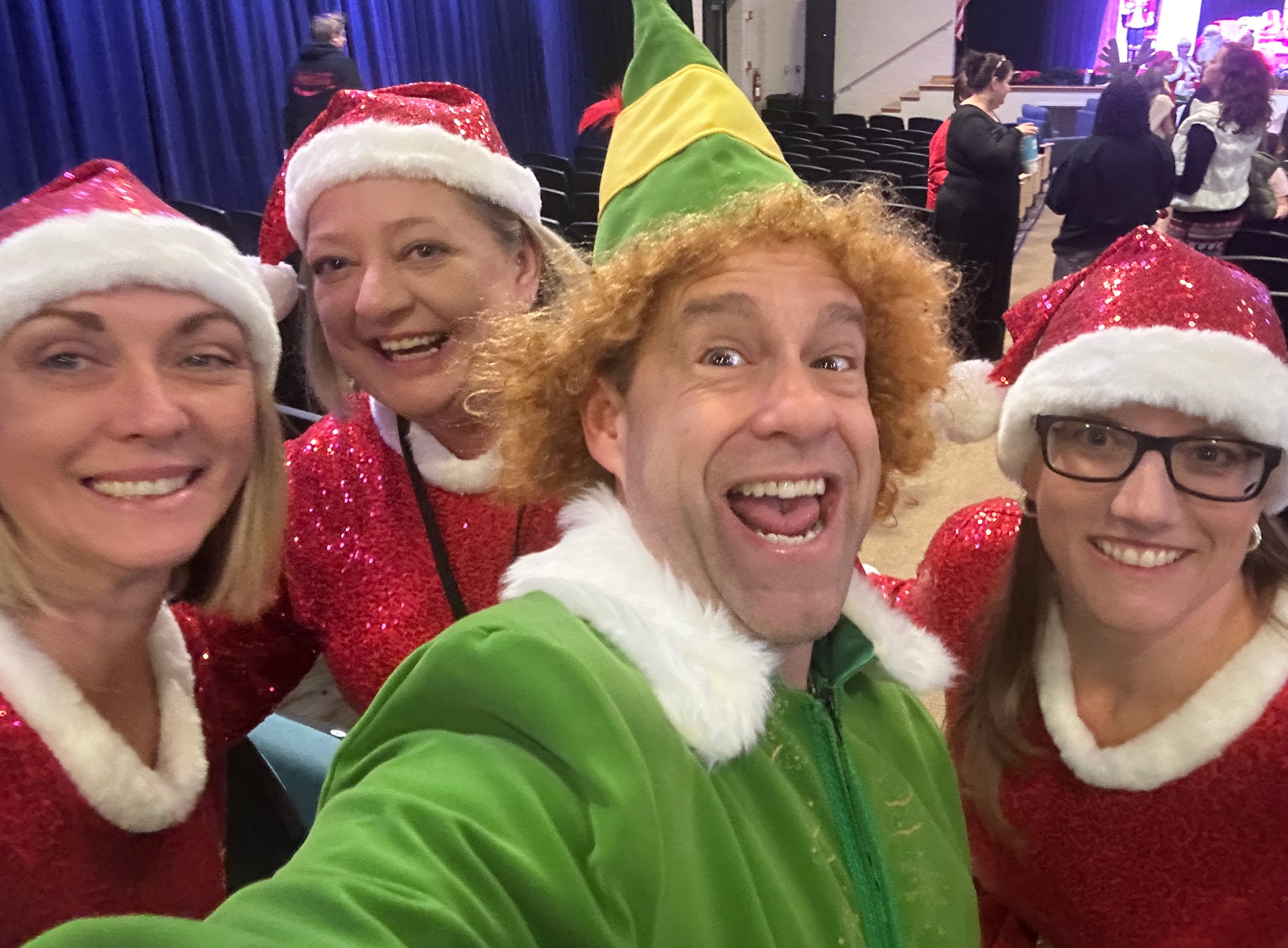 Photo of Tommy Donovan dressed as Buddy the Elf with three audience members dressed in Santa hats and matching Santa dresses