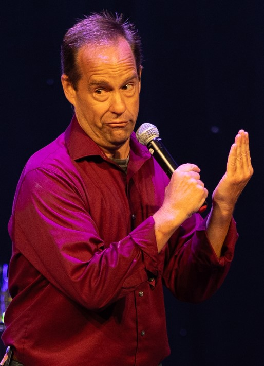 Tommy Donovan performing on stage, holding a microphone, and giving a sarcastic look to the audience.